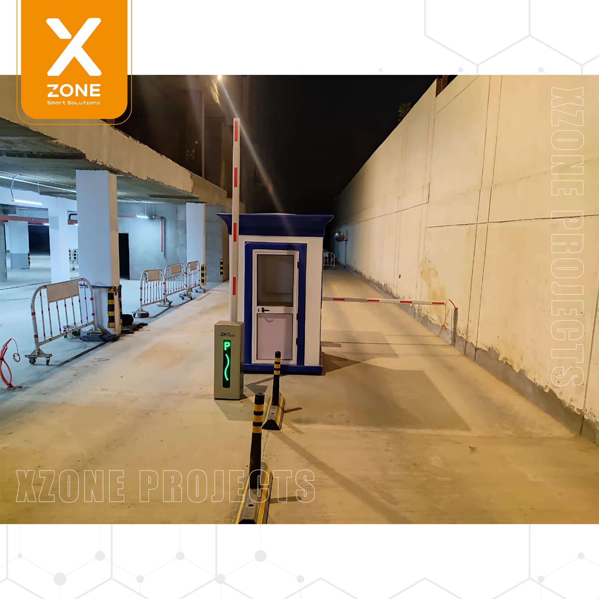 Security booth with a lowered barrier arm and digital parking sign at a concrete entrance.