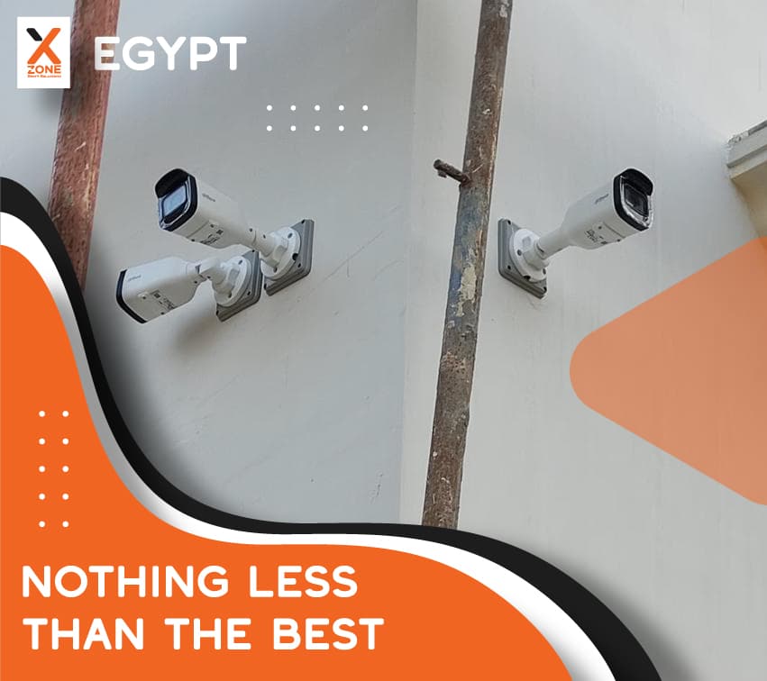Three white security cameras mounted on a wall with X Zone Egypt promotional graphics.